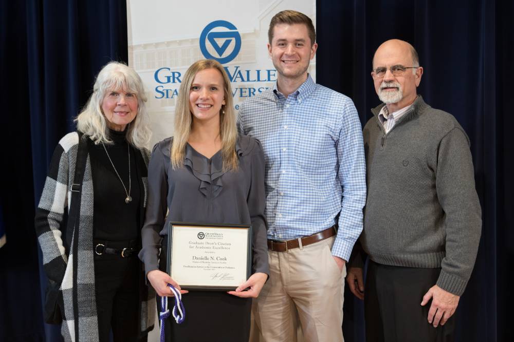 A group photo of a graduate student and her award with three of her guests